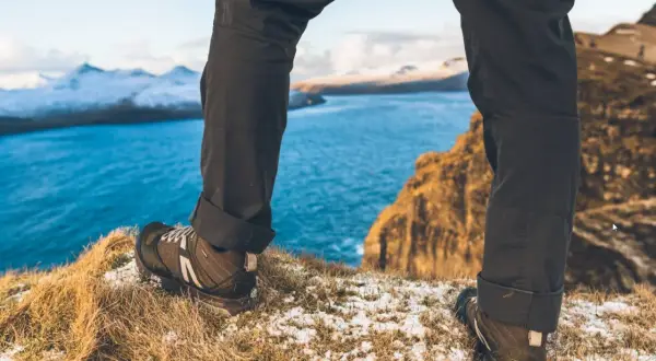 Nogi w butach trekkingowych na tle błękitnego morza i ośnieżonych gór. To prawdziwy hiking po polsku, pełen przygód i pięknych widoków.