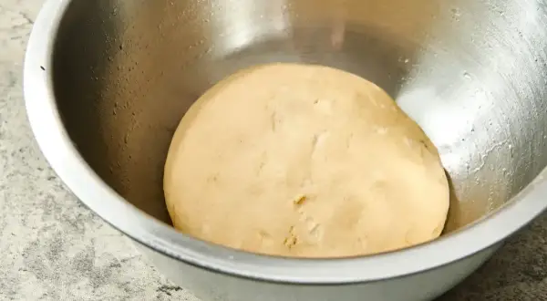 Gładkie, jasne ciasto na pizzę w metalowej misce, gotowe do wyrastania.