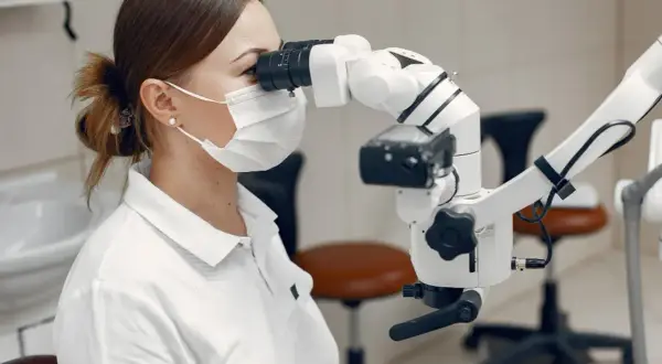 Dentystka w masce i rękawiczkach wykonuje leczenie kanałowe zęba krok po kroku, używając mikroskopu.
