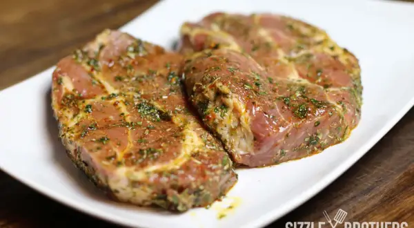Zwei saftige Steaks, mariniert mit Kräutern und Gewürzen, liegen auf einem weißen Teller. Die Frage: Steak marinieren oder nicht?