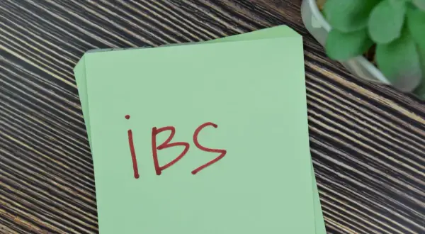 Zielona kartka z napisem "ibs" na drewnianym tle. Może to być przypomnienie o potrzebie leczenia, np. lekiem Duspatalin.
