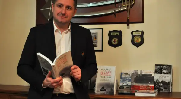 Un homme lit un livre sur l'histoire de la 1re division blindée polonaise. Le nom "Switek" pourrait être lié à l'origine de ce nom, peut-être un ancêtre ou un lieu.