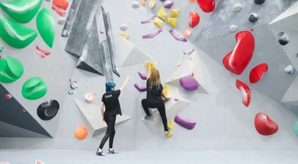 Zwei Frauen bouldern an einer Kletterwand. Eine gibt Anweisungen, die andere klettert. Das ist, was ist bouldern: eine Herausforderung für Körper und Geist.