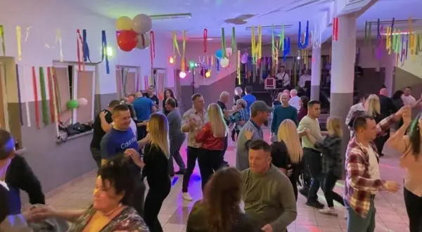 Wesoła zabawa w remizie, ludzie tańczą przy muzyce. Kolorowe serpentyny i balony tworzą świąteczną atmosferę.