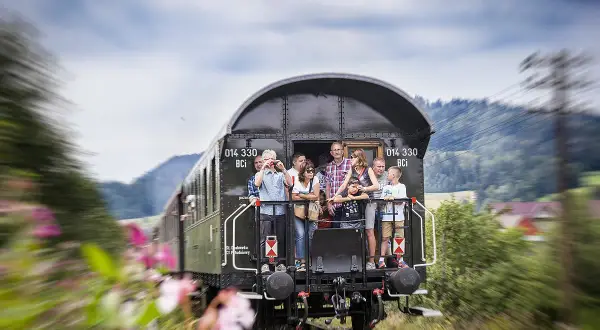 Familie genießt die Fahrt mit einem historischen Zug nach Polen. Blumen und grüne Hügel ziehen vorbei.