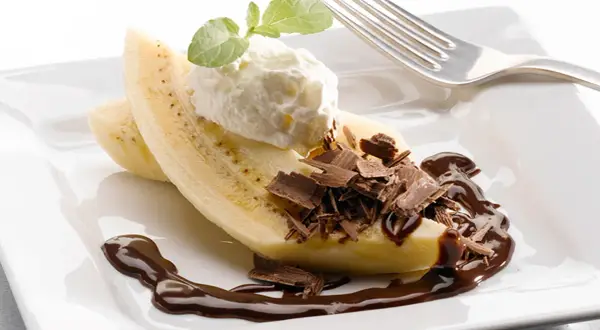 En bananhalva med vispgrädde, chokladspån och chokladsås. En klassisk banana split som ser utsökt ut.
