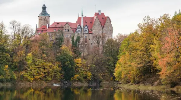 Zamek Książ w jesiennej odsłonie, idealne miejsce na jednodniowy wypad w Polsce. Otoczony kolorowymi drzewami, odbija się w spokojnej tafli wody.