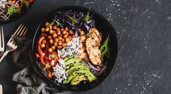 Un bol savoureux avec poulet grillé, riz, pois chiches, avocat et légumes. Parfait pour l'alimentation musculation.