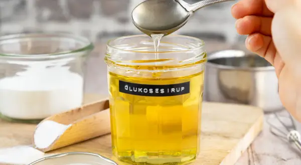 Glas mit Glukosesirup, bereit für leckere glucose rezepte. Daneben Zucker und ein Schneebesen.