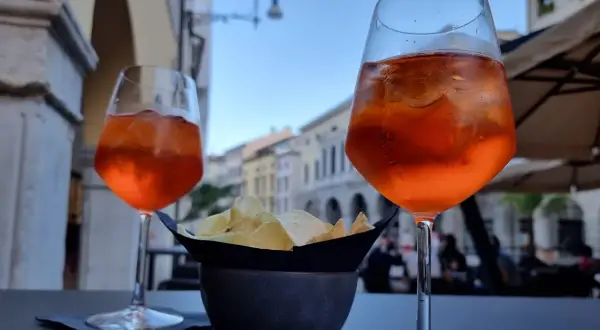 Dwa drinki Aperol Spritz i miseczka chipsów na stoliku. Czy alkohol podnosi cholesterol? To pytanie zadaje sobie wielu, popijając orzeźwiający drink.