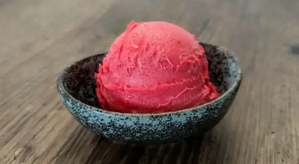 Ein Löffel Kirsch Eis in einer Schale auf Holztisch.
