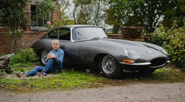 Man sitter vid en grå Jaguar E-Type i lantlig miljö.