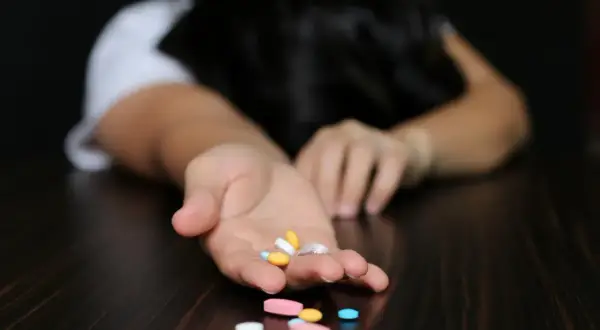 Dłoń z garścią tabletek, w tym alprazolam, na ciemnym blacie.