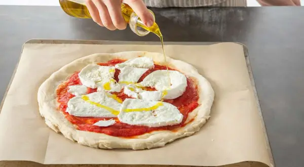 Oliwa z oliwek spływa na pizzę z mozzarellą i sosem pomidorowym, przygotowywaną w Thermomixie.