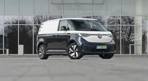 Dwukolorowy Volkswagen ID. Buzz 7 osobowy, zaparkowany przed nowoczesnym budynkiem z lustrzanymi oknami.