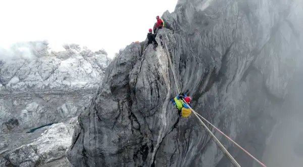 Wspinaczka na piramidę Carstensza. Alpinisci zmagają się z trudnym terenem skalnym, używając lin do asekuracji.