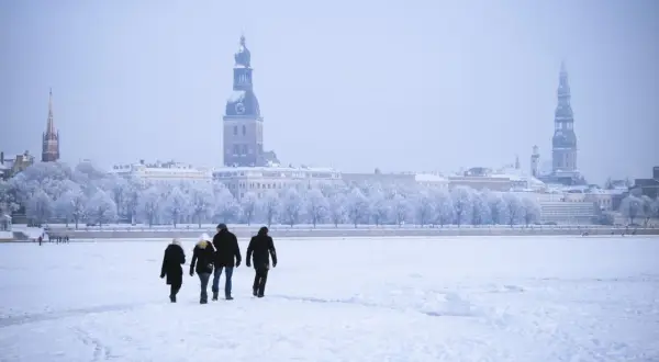 Familie spaziert über zugefrorene Daugava in Riga, Lettland im Winter. Die Stadt mit ihren Türmen ist im Schnee versunken.