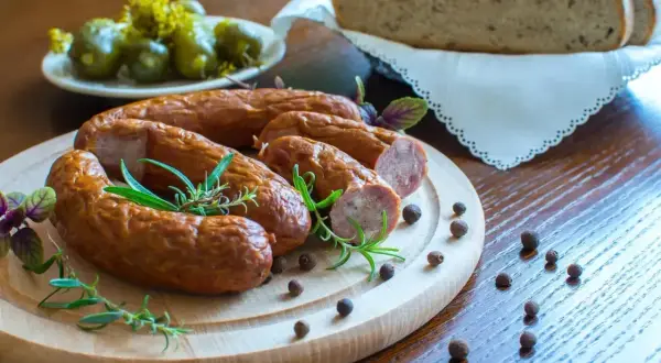 Smaczna kiełbasa na desce z rozmarynem i pieprzem. Zastanawiasz się, ile metrów jelit na 10 kg kiełbasy?