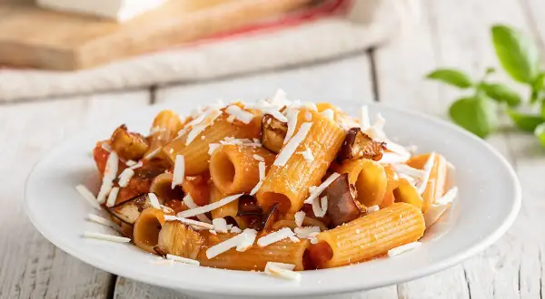 Piatto di pasta alla norma ricetta originale con melanzane fritte, pomodoro e ricotta salata grattugiata.
