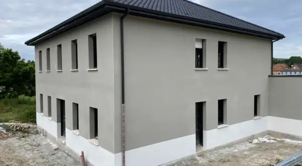 Maison neuve avec enduit de façade gris clair et soubassement blanc. Le chantier est en cours, montrant comment faire un enduit de façade.