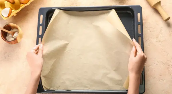 Dłonie układają papier do pieczenia na blasze. To świetne rozwiązanie, co zamiast papieru do pieczenia, gdy chcesz uniknąć przypalenia.