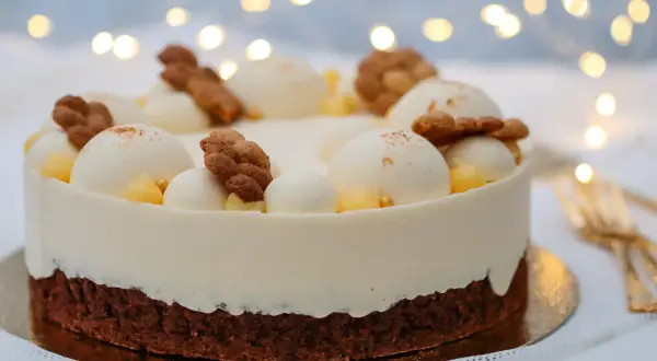 En vacker tårta med lemoncurd och chokladmousse, dekorerad med vita bollar, kex och gul topping. Bakgrunden har julbelysning.