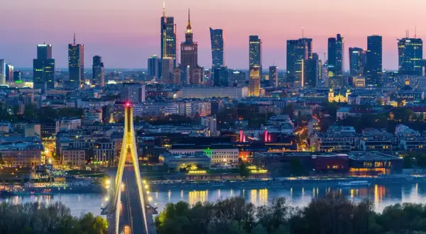 Warszawa nocą, z mostem i wieżowcami. Miasto tętni życiem, a jego warszawa liczba mieszkańców stale rośnie.