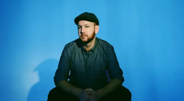 Matt Simons, nach dem Erdrutsch, sitzt nachdenklich vor blauem Hintergrund.