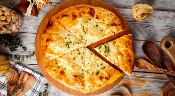Chaczapuri pokrojone w trójkąty, posypane szczypiorkiem, na drewnianej desce.