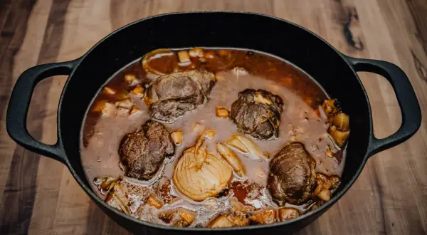 Herzhafte schmorgerichte im gusseisentopf, mit zarten Fleischrollen und Wurzelgemüse in einer dunklen Sauce.
