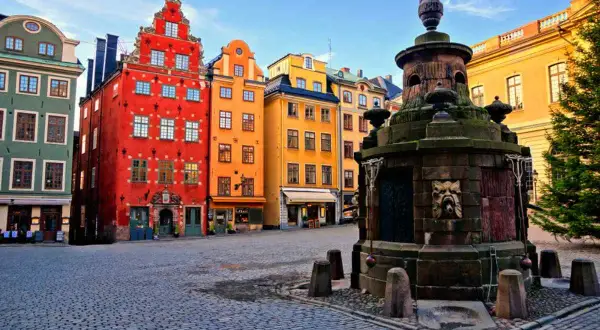 Färgglada hus i Gamla Stan, Stockholm, med en gammal fontän på kullerstensbelagd plats.