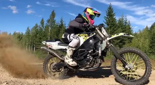Motocyklista w kolorowym kasku pędzi na crossie, wzbijając tumany kurzu.