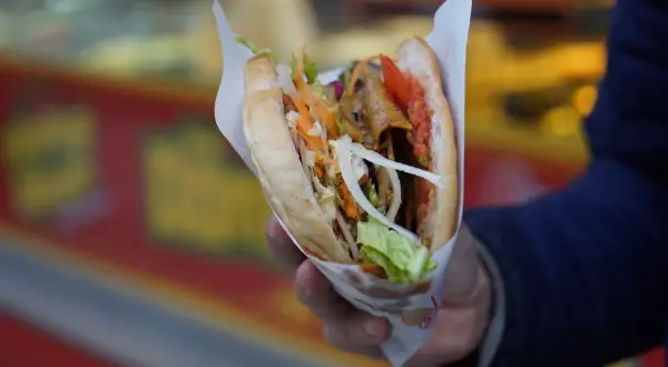 Ręka trzyma soczystego kebaba z warzywami. Czy kebab to fast food? Zdecydowanie tak, szybki i pyszny!