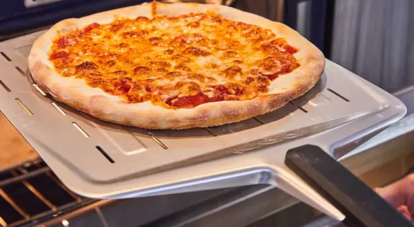 Une délicieuse pizza maison dorée et gratinée sort du four sur une pelle à pizza.