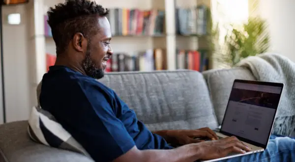 Mann auf Sofa nutzt Laptop, um mit umfragen geld verdienen steuer.