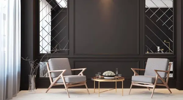 Elegancka czarna ściana w salonie aranżacje z dwoma szarymi fotelami i złotym stolikiem. Lustra w geometryczne wzory dodają głębi.