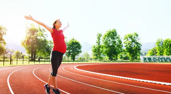 Donna incinta con le braccia aperte su una pista da corsa, dimostra che si può correre in gravidanza.