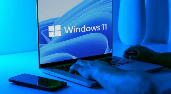 Ręce na klawiaturze laptopa z logo Windows 11. Dowiedz się, jak wejść do BIOS-u Windows 11.