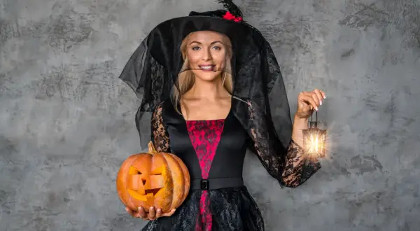 Kobieta w stroju czarownicy z dynią i latarenką. Inspiracja, jak się ubrać na Halloween.