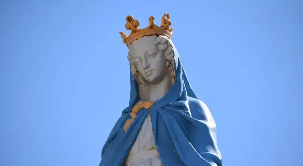 Posąg Matki Boskiej w koronie na tle błękitnego nieba.
