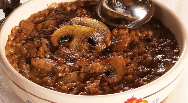 Una ciotola decorata con una ricca zuppa di farro e funghi, pronta per essere servita con un mestolo.