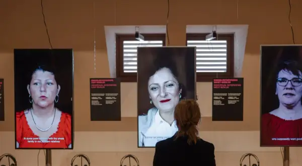 Eine Frau betrachtet drei Bildschirme mit Porträts von Frauen. Die Installation thematisiert die **Vergangenheit gegenwart** und individuelle Interviews aus Ost- und West-Berlin.