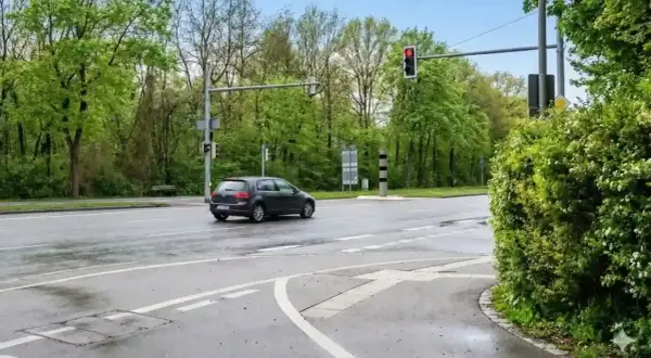 Ein dunkler Golf fährt über eine nasse Straße, die Ampel zeigt rot. Hoffentlich hat er nicht bei rot geblitzt.