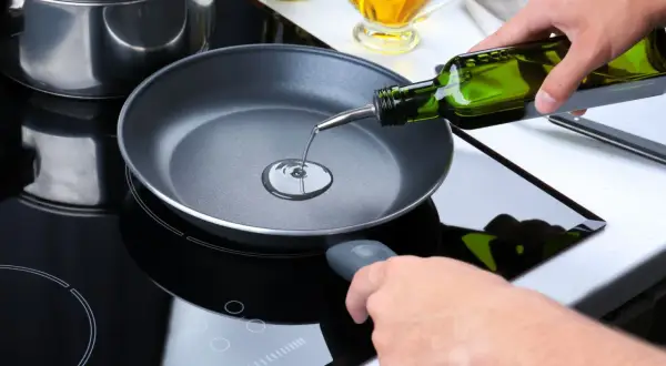Mani versano olio extravergine in una padella su un piano cottura a induzione. Si può friggere con olio extravergine per un gusto autentico.
