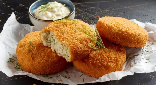 Crujientes croquetas de merluza doradas, una partida revela su interior tierno. Servidas con una cremosa salsa y eneldo fresco.