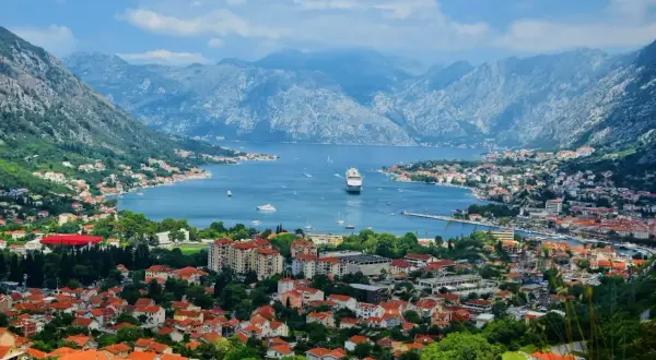 Vacker vy över Kotorbukten i Montenegro. Ett kryssningsfartyg ligger för ankar i det blå vattnet, omgivet av berg och en stad med röda tak. Montenegro mat kan avnjutas med en sådan här utsikt.