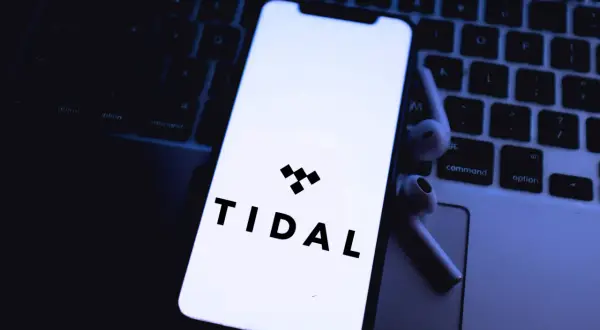 Smartfon z logo Tidal na klawiaturze laptopa i słuchawkami bezprzewodowymi.