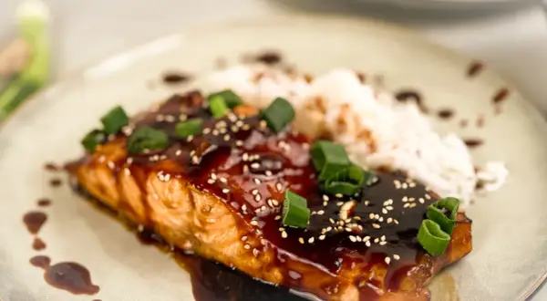 En saftig asiatisk lax med glansig teriyakisås, toppad med sesamfrön och salladslök, serveras med ris.
