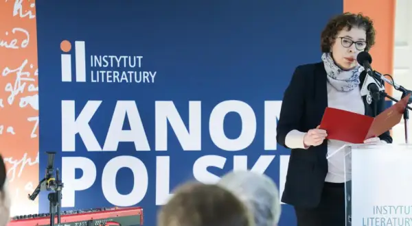 Kobieta przemawia na tle napisu "Instytut Literatury" i "Kanony Polskie", prezentując dzieła najwybitniejszych polskich pisarzy.