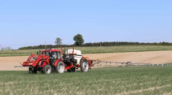 Czerwony traktor z opryskiwaczem na polu. Prawidłowa kolejność mieszania środków ochrony roślin zapewnia skuteczne działanie.